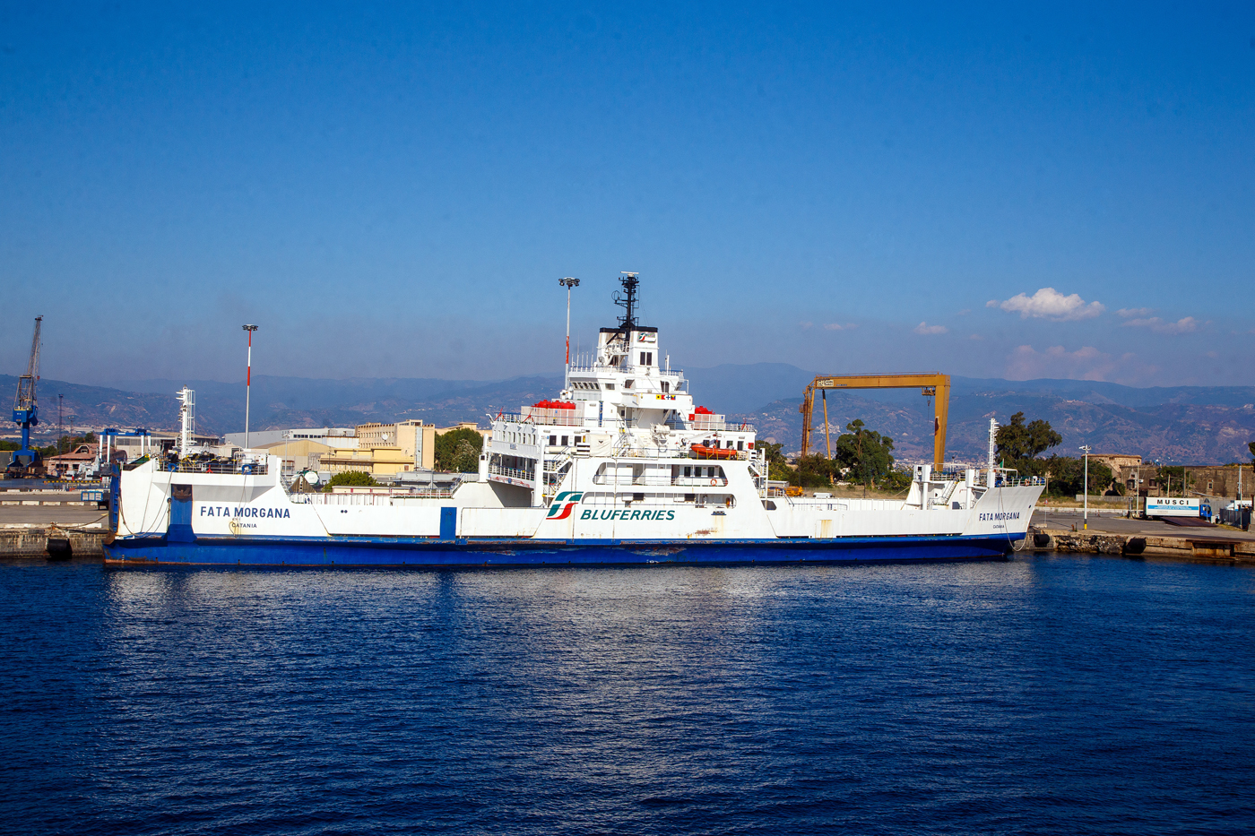Die FATA MORGANA (IMO 8506543) ein Ro-Ro Fährschiff der Bluferries (ein Unternehmen der Gruppe FS - Ferrovie dello Stato Italiane), liegt am 20.07.2022 beim Fährterminal von Messina. Diese Fähre ist für die Beförderung von Passagieren und Radfahrzeugen in der Straße von Messina. Sie kann aber auch Eisenbahnwaggons transportieren (Trajekt). 

TECHNISCHE DATEN:
Bauwerft: Fincantieri – Cantieri Navali Italiani S.p.A. in Livorno, Italien
Kiellegung/Stapellauf: 1887 / 1988
Inbetriebnahme: 1989
Vermessung (Bruttoraumzahl): 2.377 BRT
Länge: 102 m
Breite: 18,82 m
Tiefgang: 4,5m
Antrieb: 2 GMT(Grandi Motori Trieste) 4-Zylinder-Dieselmotoren mit einer Leistung von 10.357 kW
Geschwindigkeit: 15,2 Knoten (28,15 km/h)
Ladekapazität: 79 Autos oder 24 LKW oder 12 Eisenbahnwaggons
Besatzung: 10
Zugelassene Passagierzahl: 500 
